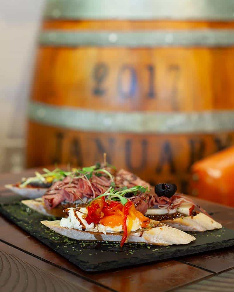 Montaditos Spanish tapas on a slate platter atop a wooden table with a wine barrel in the background