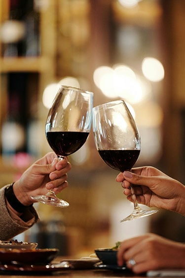 Two adults toasting red wine over a table of tapas at UnWINEd Wine & Beer Bar